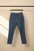 A pair of blue denim jeans hanging from white plastic hangers against a beige fabric backdrop.
