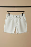 A white denim mini skirt with front slash pockets and a button closure, hanging on a wooden hanger against a dark red background.