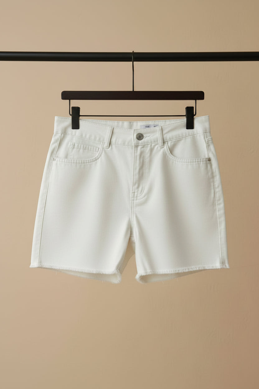 A white denim mini skirt with front slash pockets and a button closure, hanging on a wooden hanger against a dark red background.
