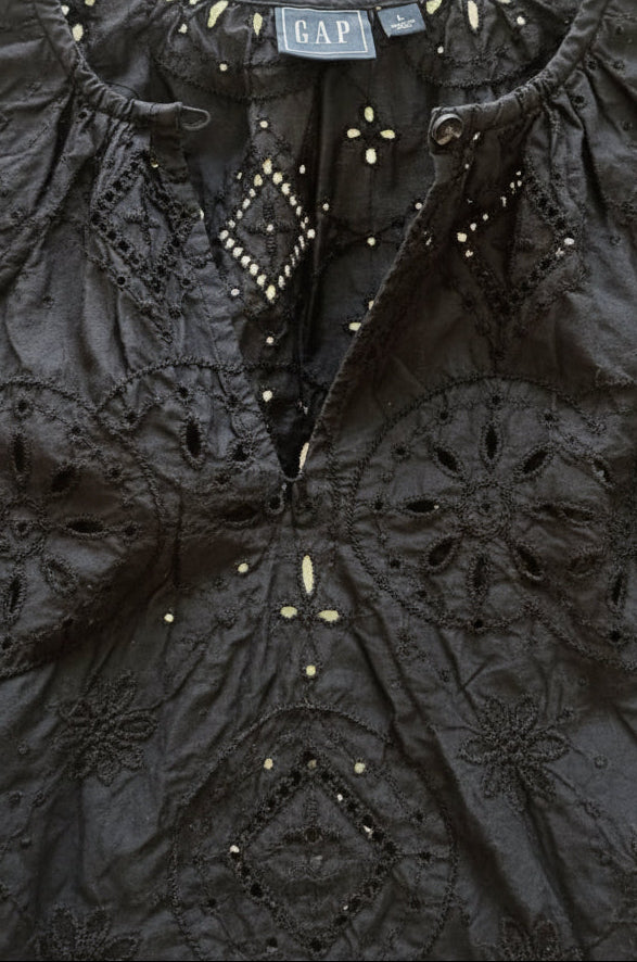 Close-up of a black lace and embroidered Gap garment hanging on a wooden hanger, with the GAP brand label visible at the neckline.