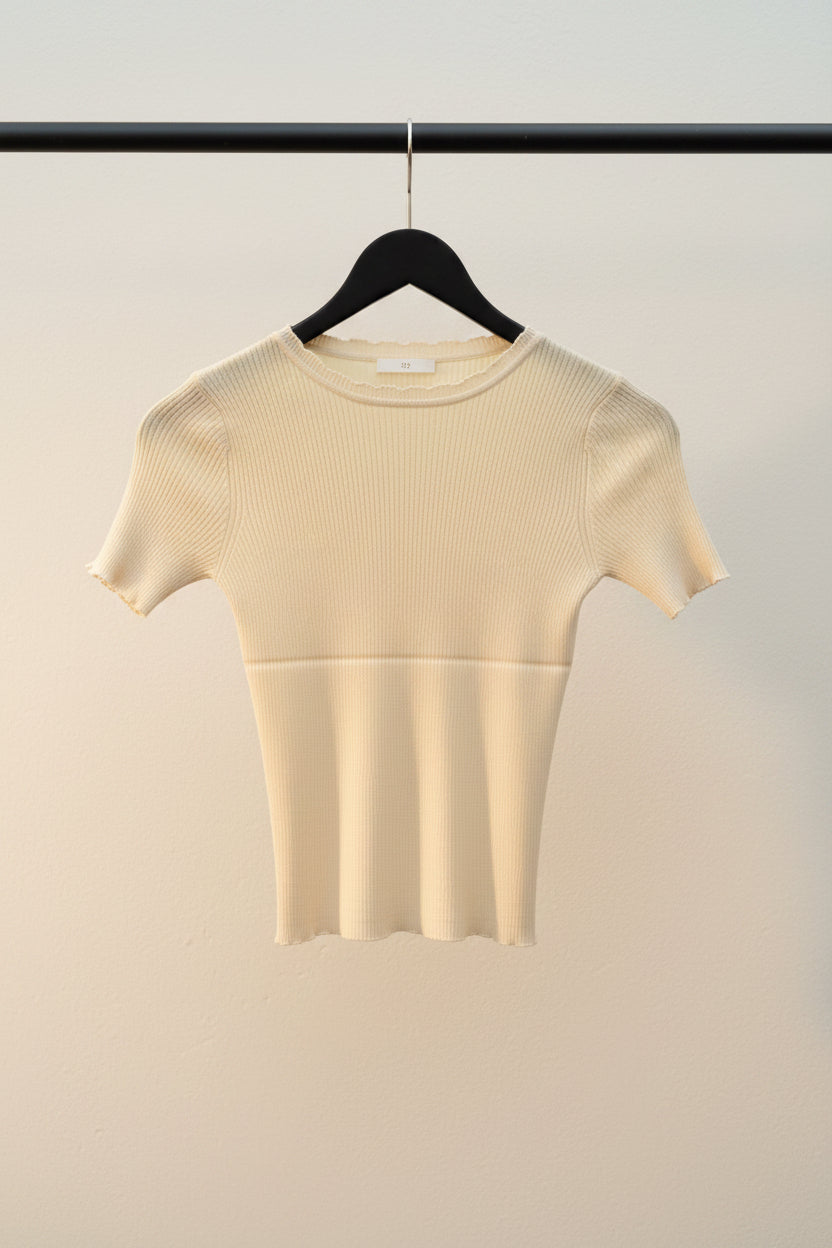 A pale yellow short-sleeve ribbed knit top hanging on a wooden hanger against a light fabric backdrop.