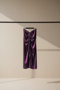 A draped purple satin or silk garment hanging from a wooden clothesline in an outdoor courtyard with potted plants and tree branches visible in the background.