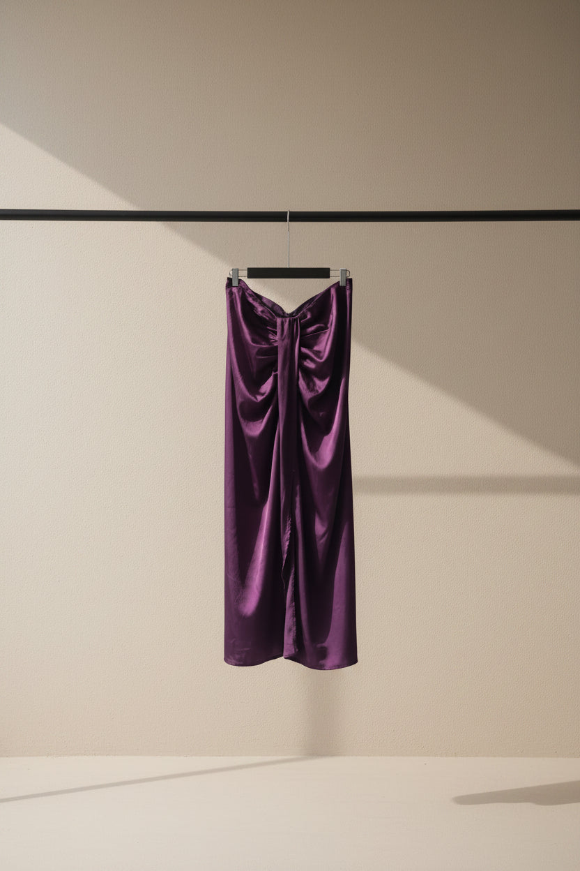 A draped purple satin or silk garment hanging from a wooden clothesline in an outdoor courtyard with potted plants and tree branches visible in the background.