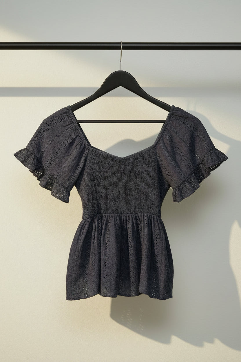 A dark navy blue eyelet lace blouse with puffed sleeves and a smocked bodice, laid flat on a light off-white background.