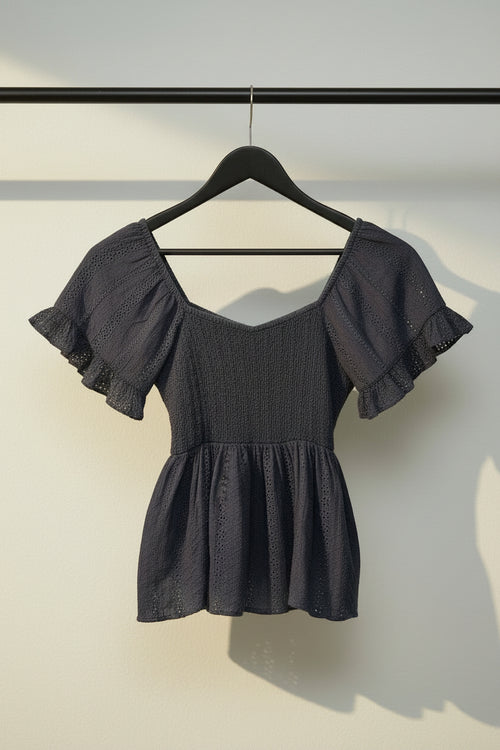 A dark navy blue eyelet lace blouse with puffed sleeves and a smocked bodice, laid flat on a light off-white background.