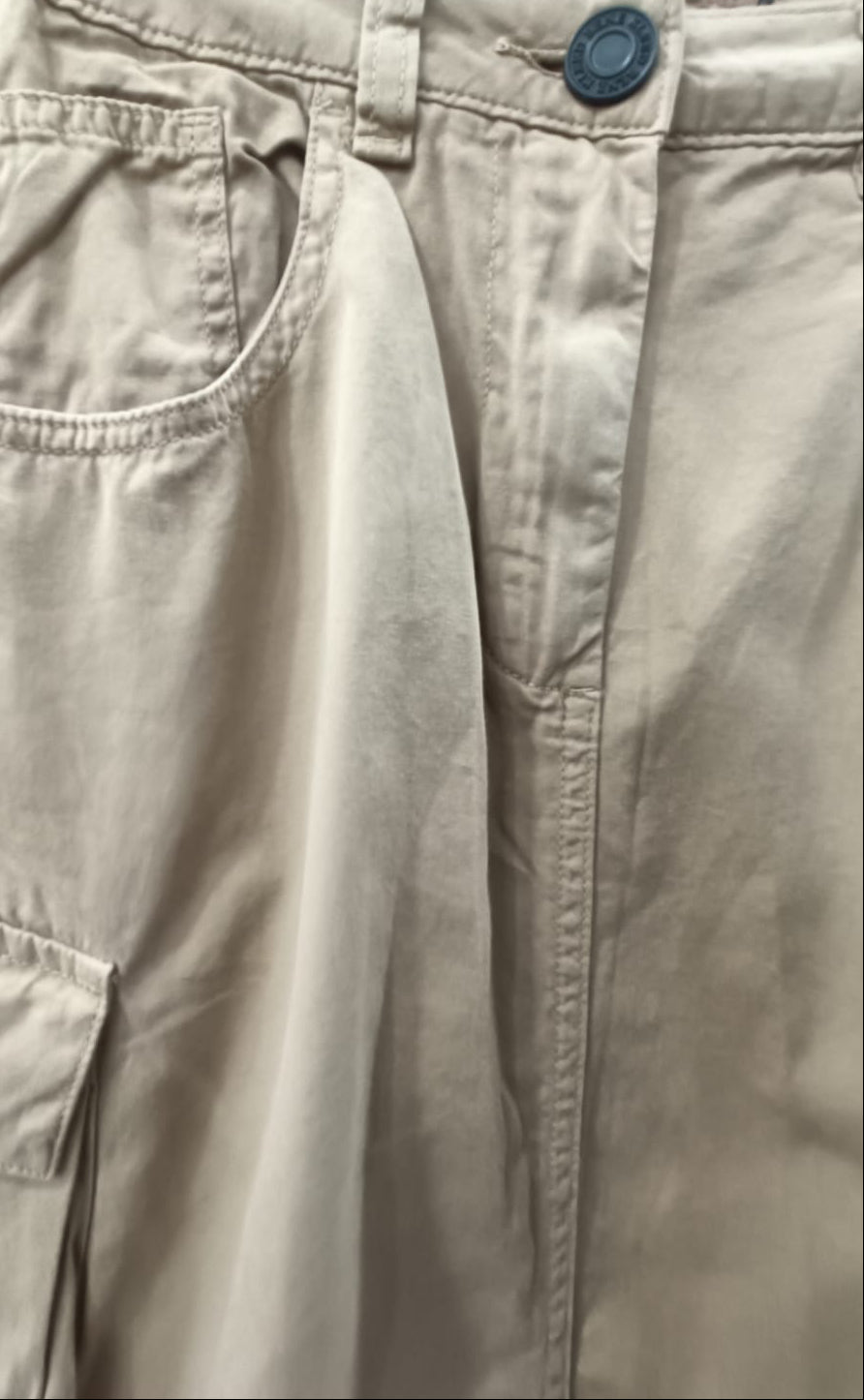 Close-up of khaki cargo pants hanging on a hanger against a dark red background, showing the waistband, belt loops, front pocket, and cargo pocket.