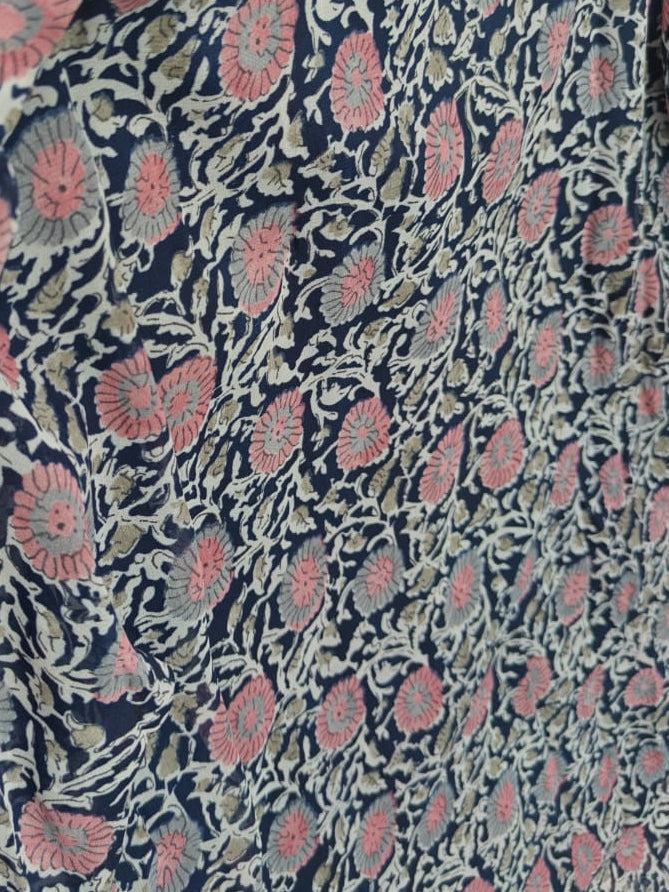 A close-up of a navy blue fabric with a pink and gray floral block print pattern, showing a ruffled sleeve detail.