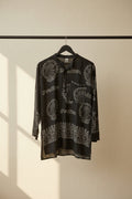 A black long-sleeve tunic top with white printed patterns and Devanagari text, laid flat on a white fabric background.
