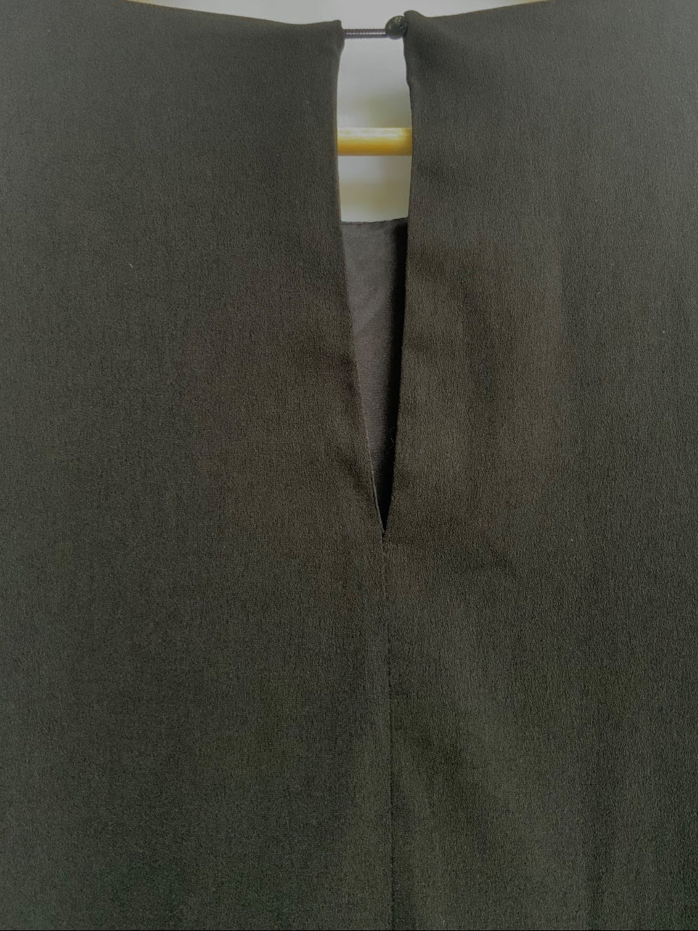 A close-up of a dark gray or charcoal-colored garment hanging on a light wood hanger, showing a split V-neckline detail.
