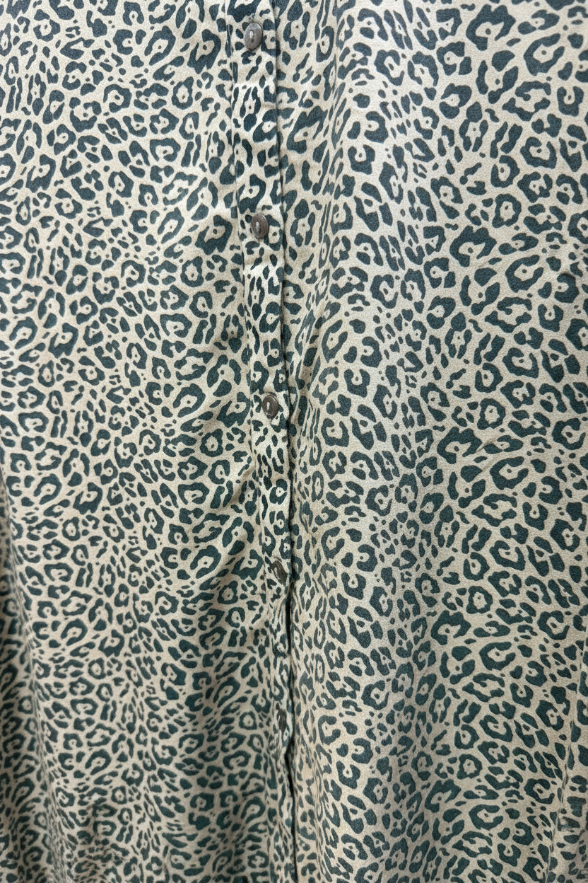 Close-up of a leopard print fabric with a beige base and dark gray spots, showing the texture and pattern details.