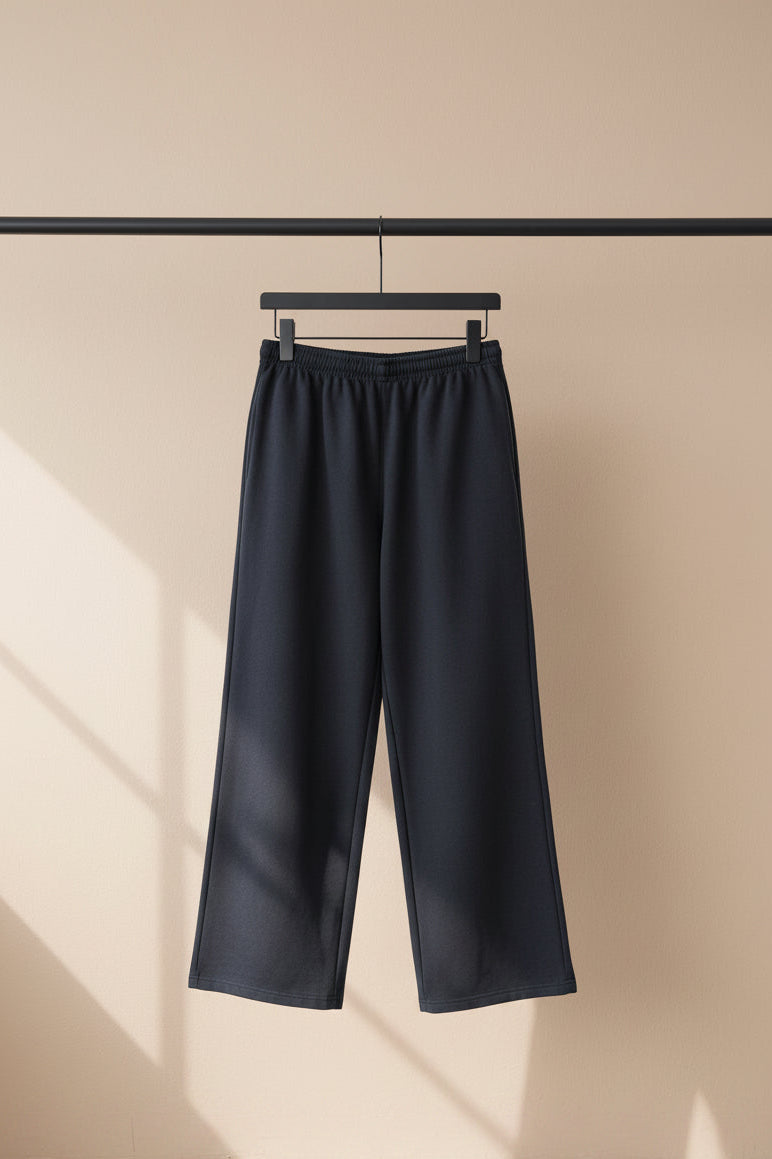 Dark gray wide-leg sweatpants with a white graphic print on the side, hanging against a light gray fabric backdrop.