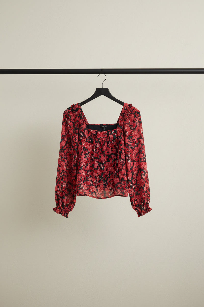 A red and black floral print long-sleeve blouse with a square neckline and ruffled cuffs, laid flat on a white fabric background.