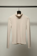 A long-sleeve white turtleneck top hanging on a wooden hanger against a neutral gray background.