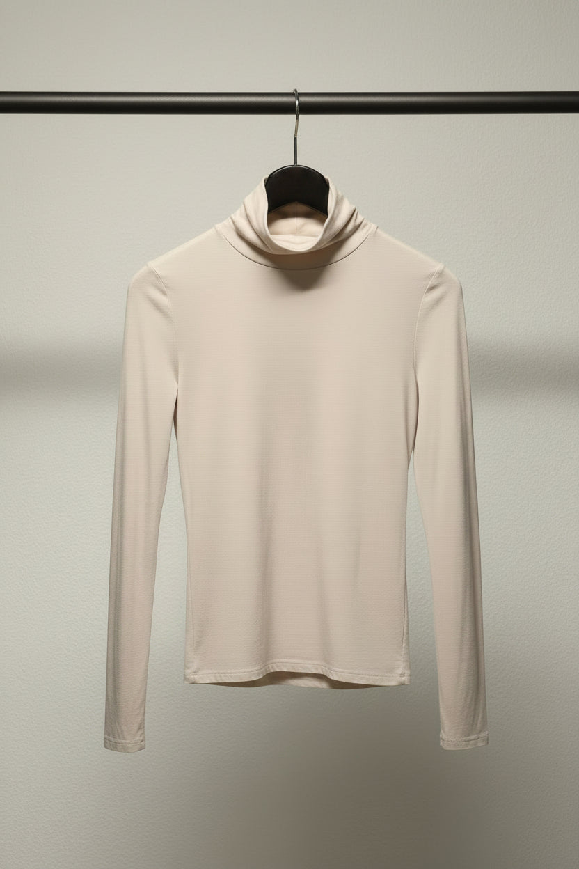 A long-sleeve white turtleneck top hanging on a wooden hanger against a neutral gray background.