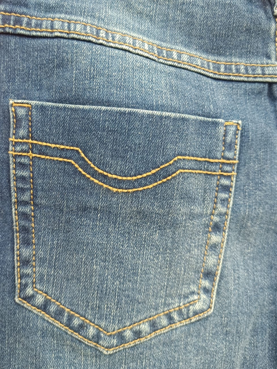 Close-up of the back pocket of blue denim jeans with contrast yellow stitching, laid flat against a red background.