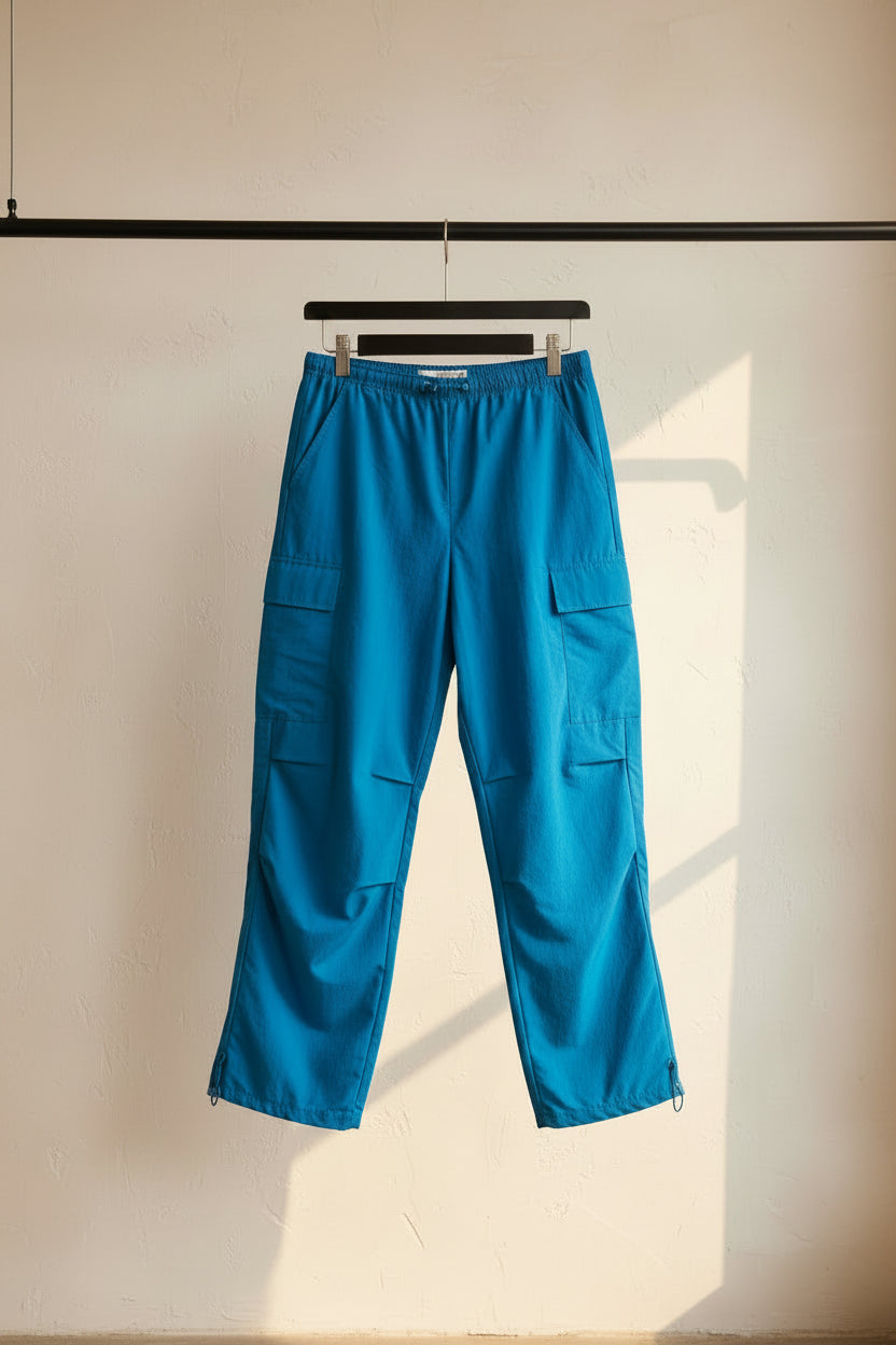 Bright blue cargo pants with multiple flap pockets, hanging on a black hanger against a neutral gray fabric backdrop.