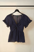 A navy blue eyelet lace top with ruffled short sleeves, a twisted front knot, and a flared peplum hem, laid flat on a light background.