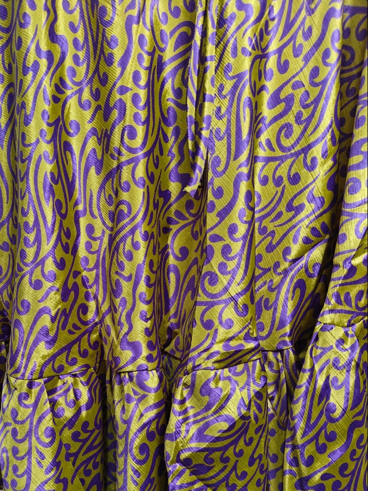 A close-up of a ruffled skirt or fabric panel featuring a bold purple and olive-yellow swirling pattern.