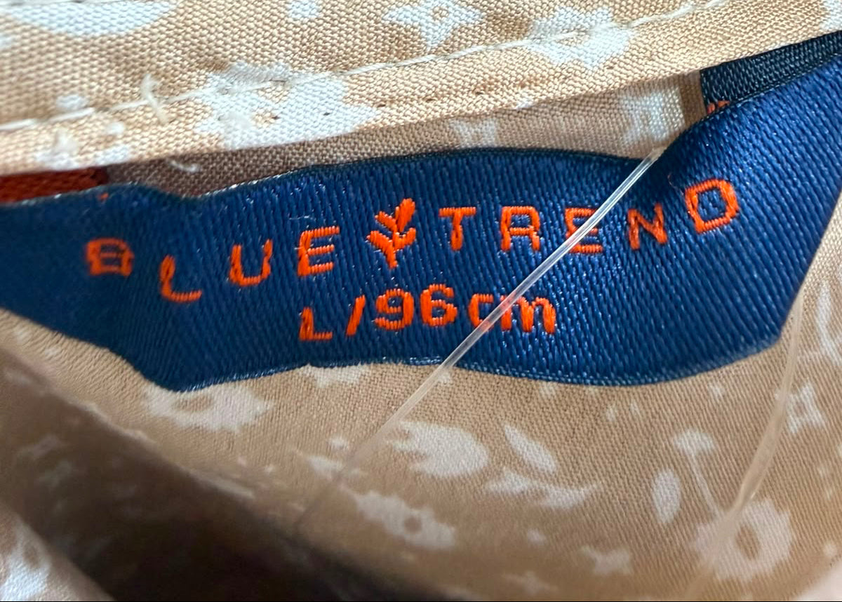 Close-up of a beige fabric garment with a white floral print and a blue sewn-in label reading BLUE TRENO.