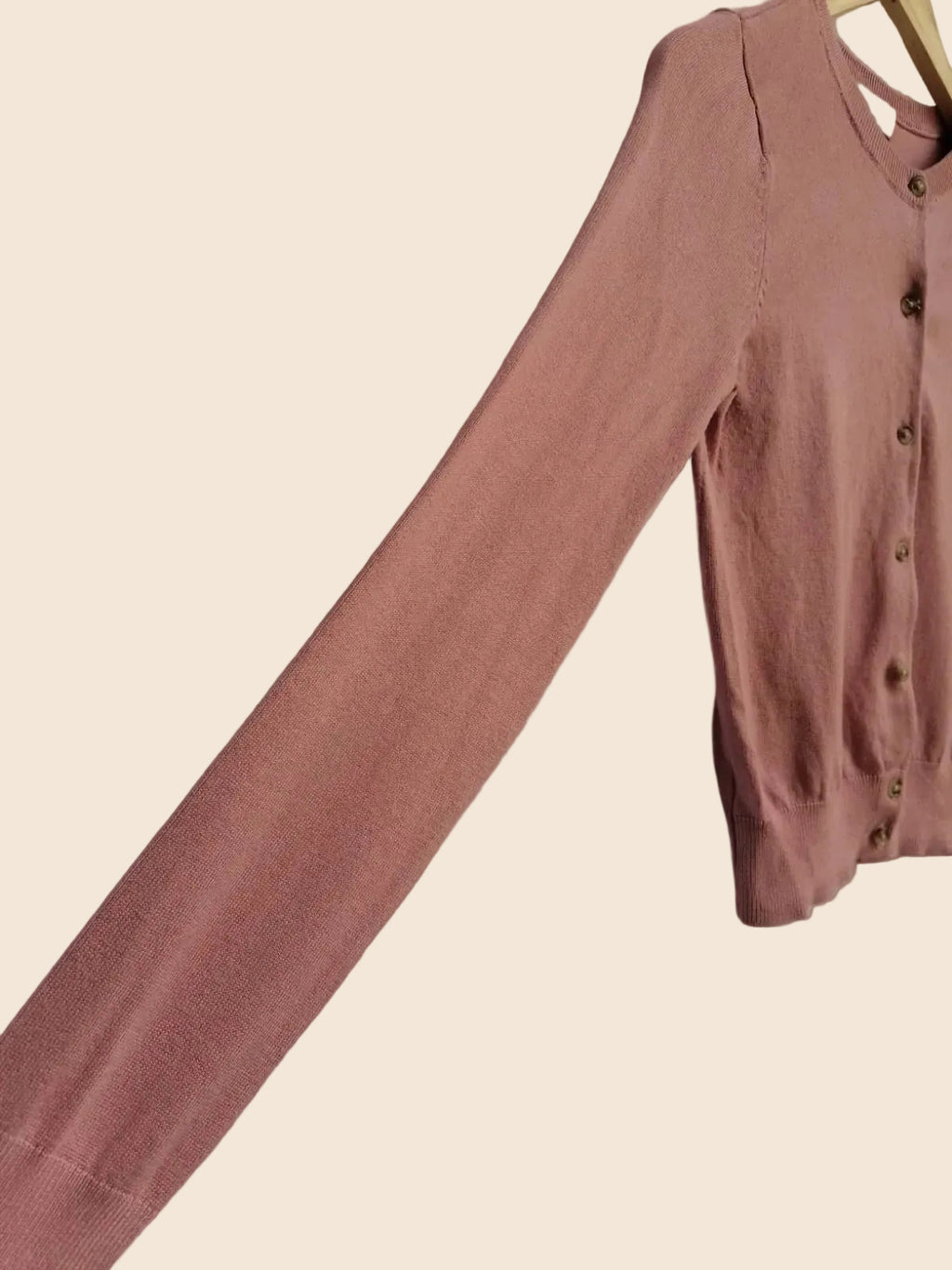 A dusty rose pink long-sleeve button-up cardigan sweater laid flat on a white fabric background.