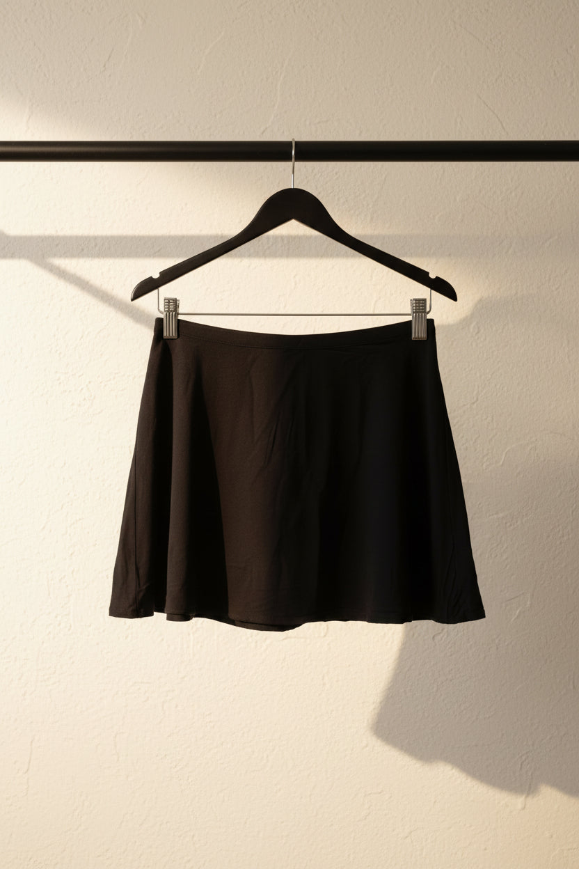 A black A-line mini skirt hanging from a wooden hanger against a neutral gray fabric backdrop.