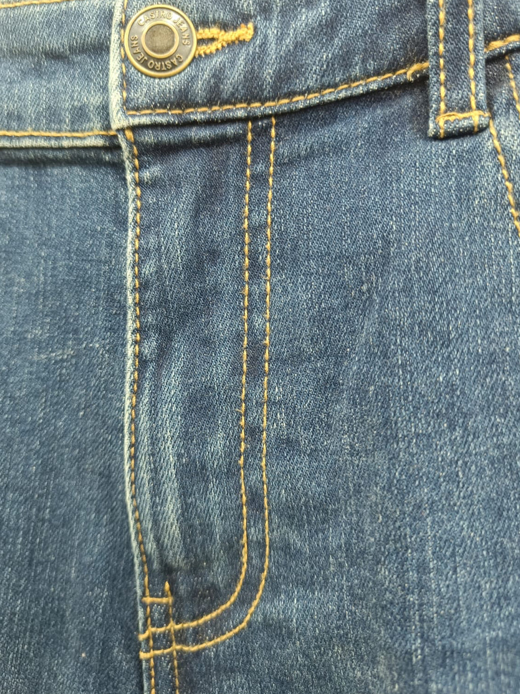 Close-up of blue denim jeans showing the waistband, button closure, belt loops, front seam, and yellow contrast stitching.