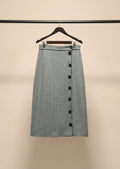 A black and white micro-checkered midi skirt with a button-down front, hanging on a wooden hanger outdoors on a tree branch.