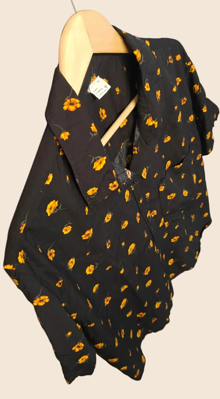 A black short-sleeve button-up shirt with a yellow leaf print, hanging on a wooden hanger against a gray wall.