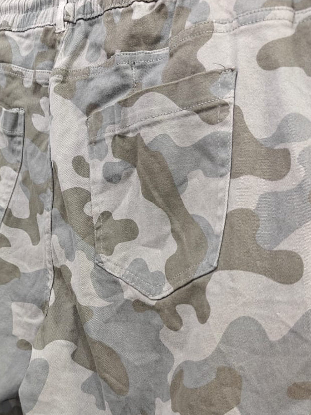 Close-up of the back of a pair of camouflage cargo pants hanging on a hanger, showing an elastic waistband, two back patch pockets, and a side cargo pocket.