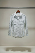A long-sleeve button-up shirt with a white base and an all-over small black monogram pattern, hanging on a wooden hanger against a charcoal background.