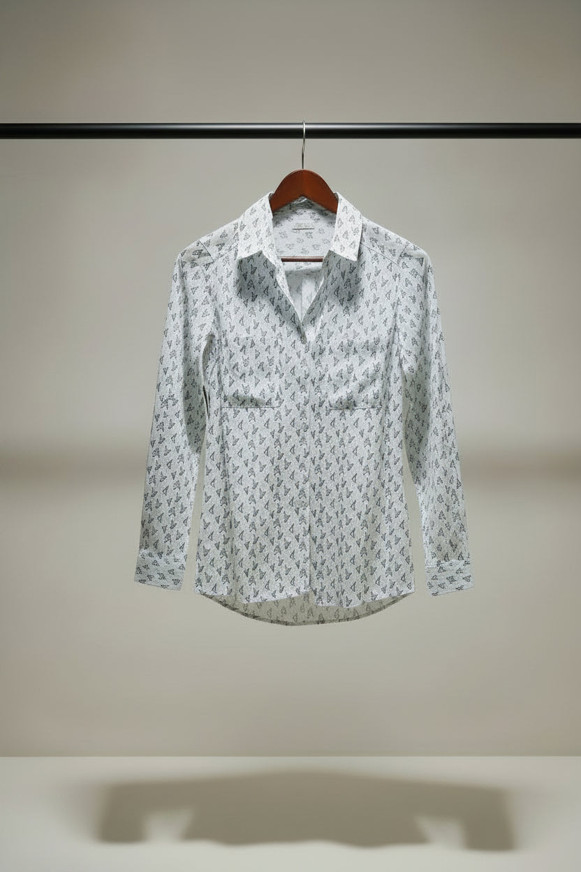 A long-sleeve button-up shirt with a white base and an all-over small black monogram pattern, hanging on a wooden hanger against a charcoal background.