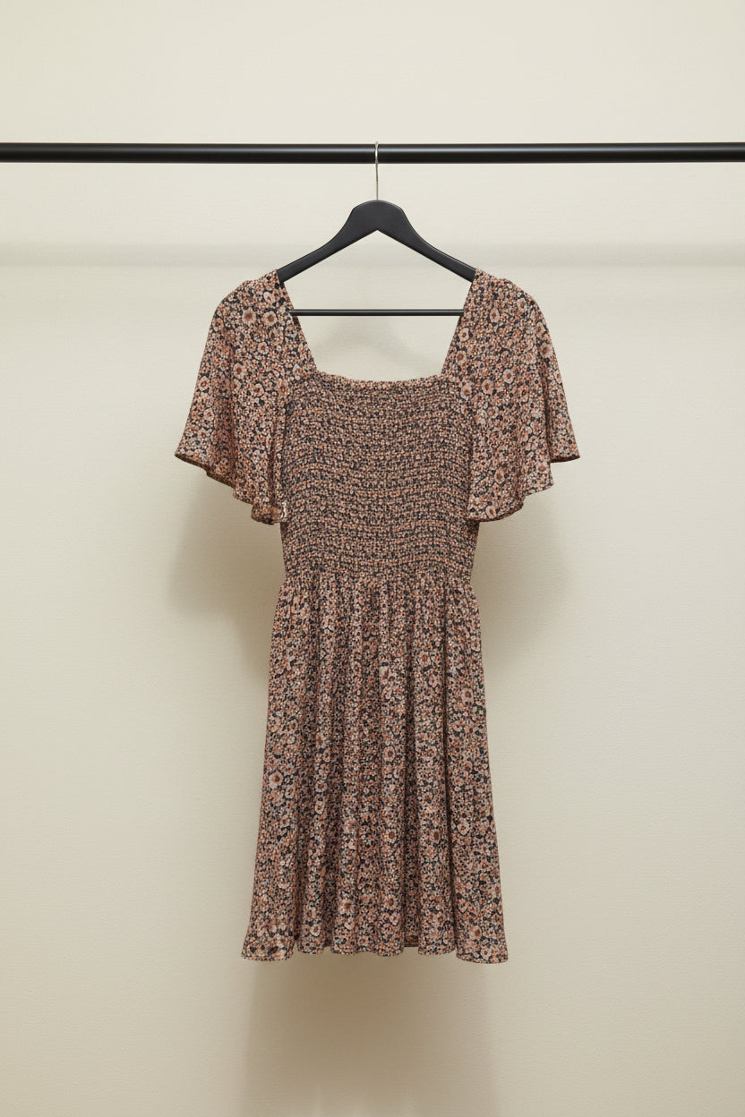 A short-sleeve floral dress with a smocked bodice and flared skirt, laid flat on a light gray background.