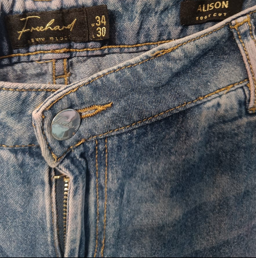 Close-up of the waistband of a pair of blue denim jeans, showing the 'Freeland' and 'Alison' brand labels, size 34/30, with a metal button and contrast stitching.
