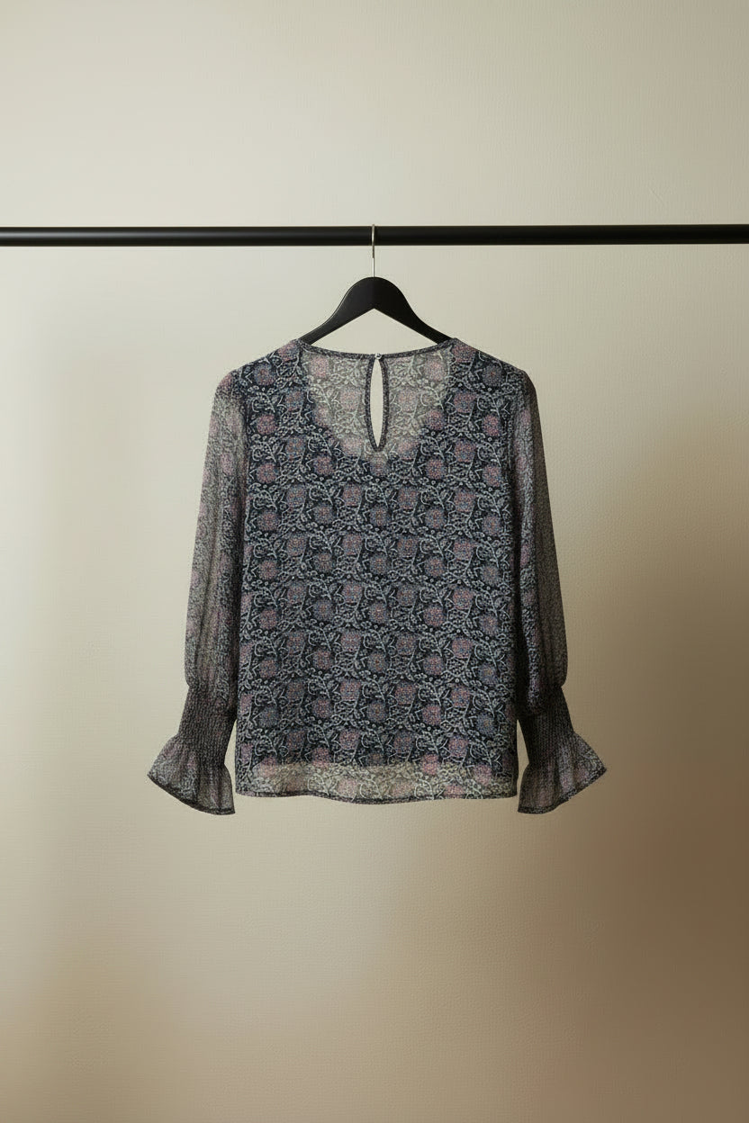 A women's long-sleeve blouse with a dense abstract geometric pattern in pink, purple, and white, laid flat on a white fabric background.