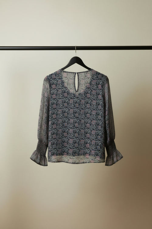 A women's long-sleeve blouse with a dense abstract geometric pattern in pink, purple, and white, laid flat on a white fabric background.