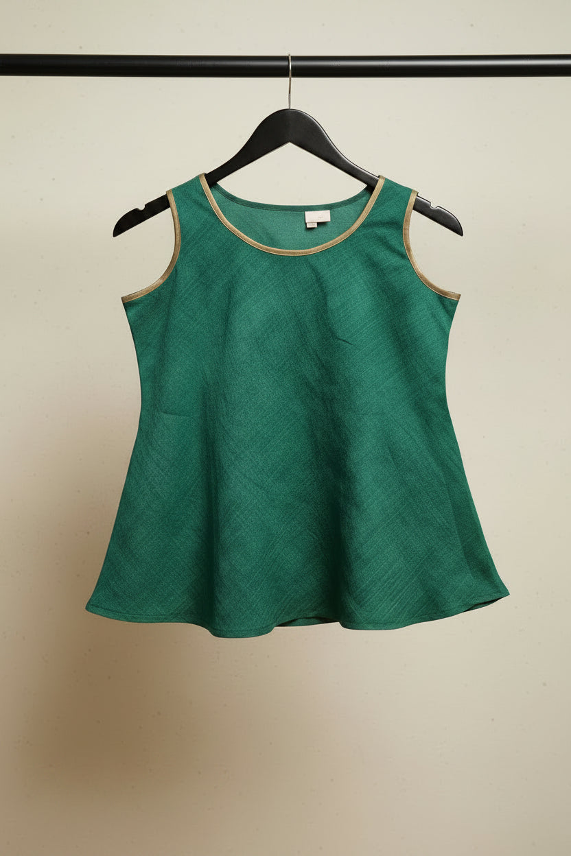 A green sleeveless top with gold trim on the neckline, hanging on a wooden hanger against a white fabric background.