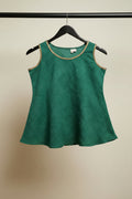 A green sleeveless top with gold trim on the neckline, hanging on a wooden hanger against a white fabric background.