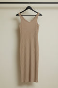 A sleeveless ribbed knit midi dress in a warm beige/tan color, hanging on a wooden hanger against a wrinkled white fabric backdrop.