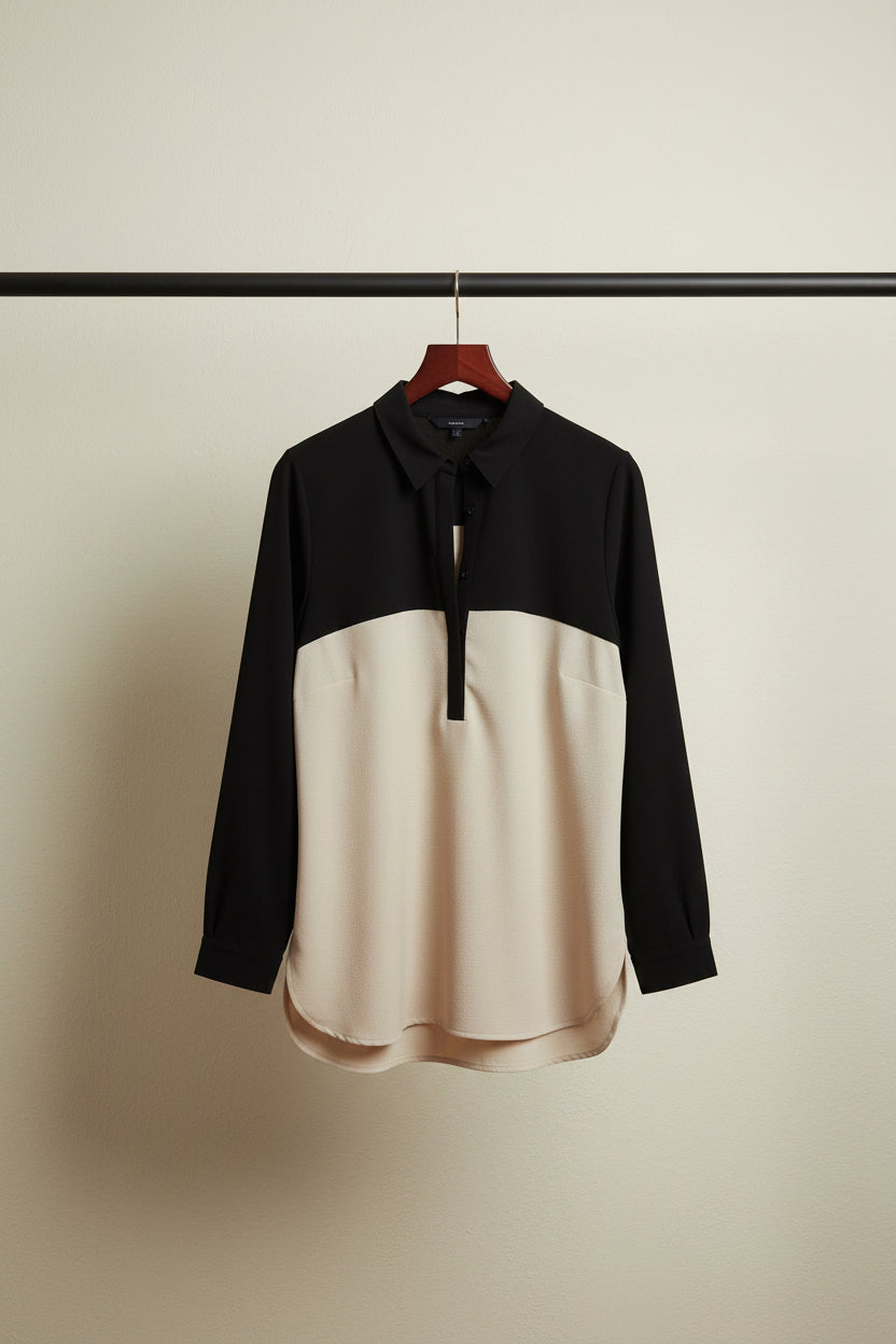 A long-sleeve colorblock polo shirt with a black upper section and sleeves, and a cream-colored lower body, laid flat on a white fabric background.
