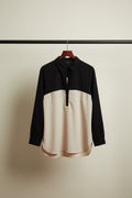 A long-sleeve colorblock polo shirt with a black upper section and sleeves, and a cream-colored lower body, laid flat on a white fabric background.