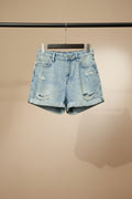 Light wash blue distressed denim shorts with rolled hems, displayed on a wooden hanger against a solid red background.