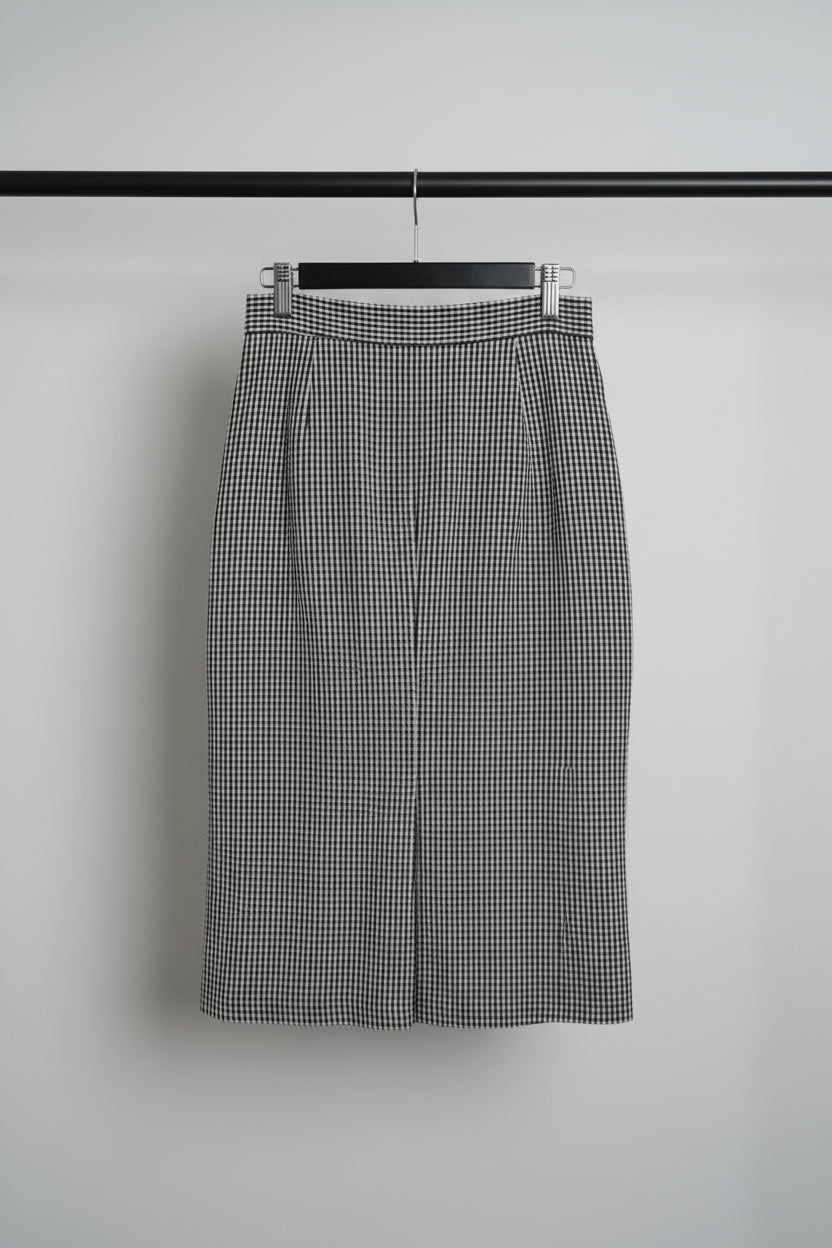 A black and white gingham check skirt with a vertical row of large black buttons down the front, hanging on a wooden hanger.