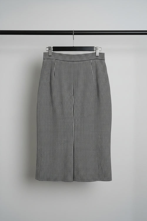 A black and white gingham check skirt with a vertical row of large black buttons down the front, hanging on a wooden hanger.