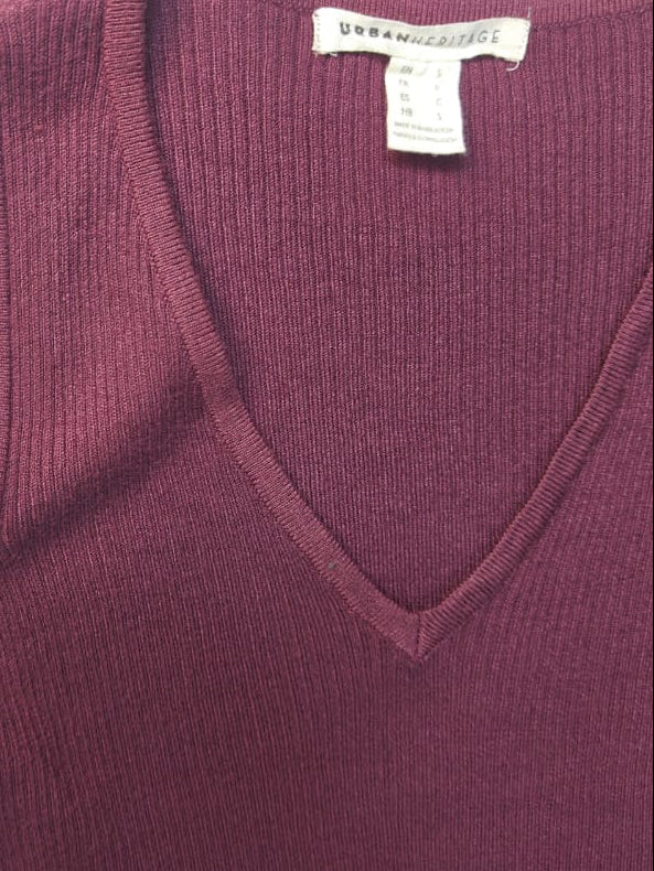 A close-up of a ribbed knit sweater in a deep plum or burgundy color, featuring a V-neckline and a shoulder cutout. A white tag inside the collar reads 'URBAN AESTHETICS'.