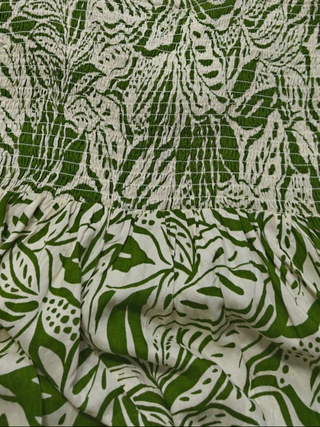A sleeveless spaghetti-strap dress with a green and off-white botanical leaf pattern, laid flat on a white background.