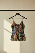 A sleeveless halter-neck swimsuit with a vibrant tropical floral print on a dark navy blue base, laid flat on a light off-white background.