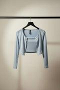 A light blue cropped cardigan with long sleeves and a scoop neckline, hanging on a wooden hanger against a dark gray background.