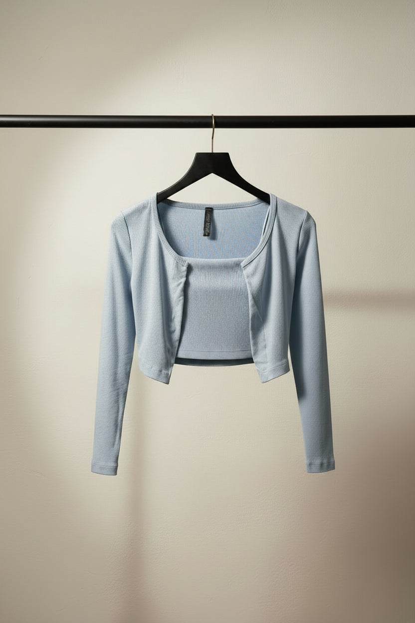 A light blue cropped cardigan with long sleeves and a scoop neckline, hanging on a wooden hanger against a dark gray background.