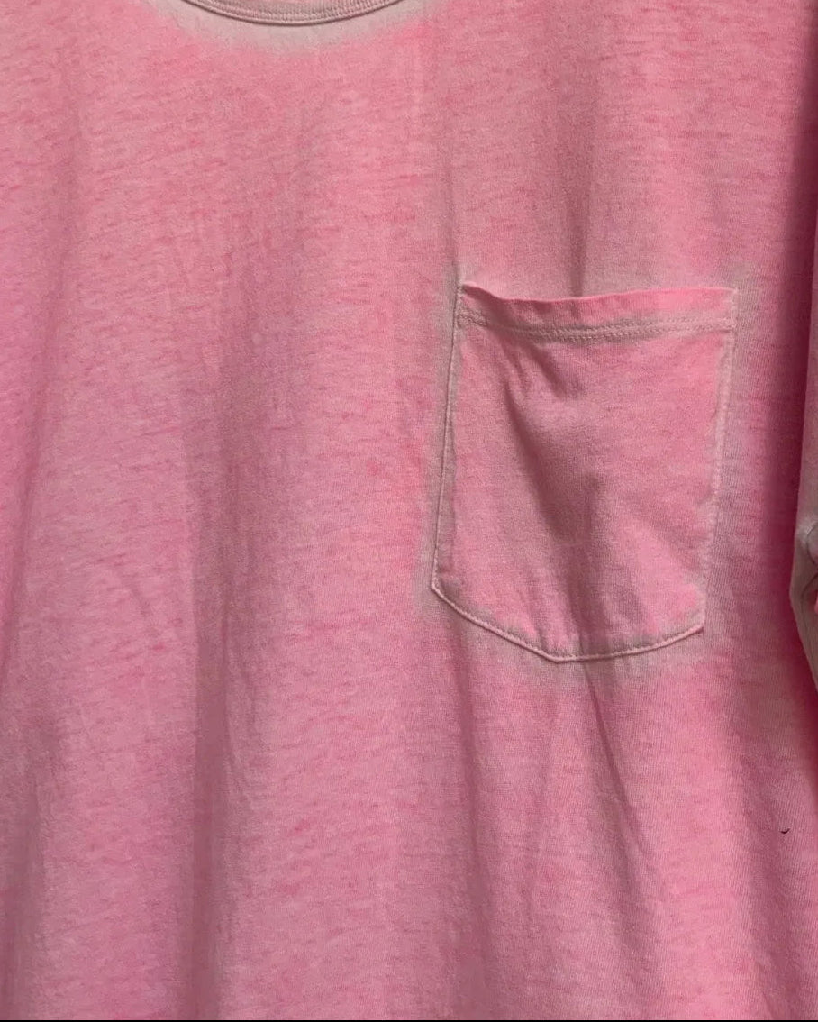A pink short-sleeve crewneck t-shirt with a chest pocket, hanging on a wooden hanger against a white fabric background.