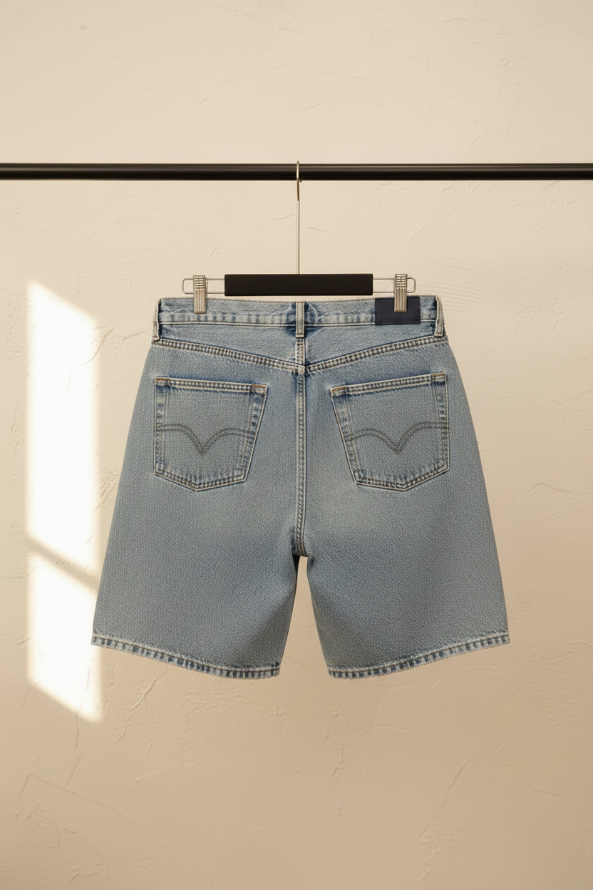 Light blue denim shorts shown from the back, hanging on a wooden hanger against a dark red background.